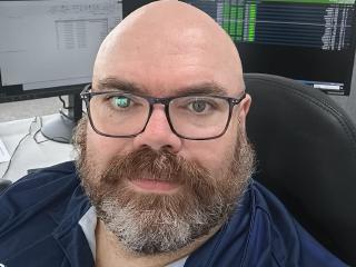 Nick in a blue polo shirt sitting in front of computer screens showing timing information